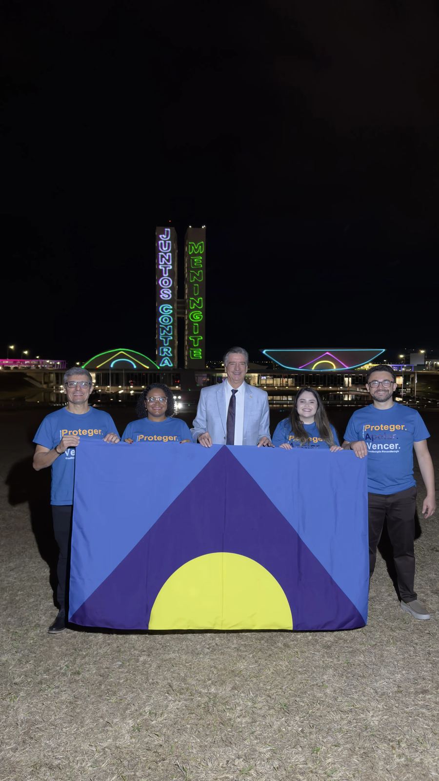 Equipe da ABCM segurando a bandeira do combate à meningite em frente ao Congresso Nacional